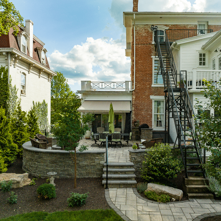Flagstone walkway, exterior stairs to the patio adjoining red brick building with balconies and 2 story iron staircase, including green shrubs
