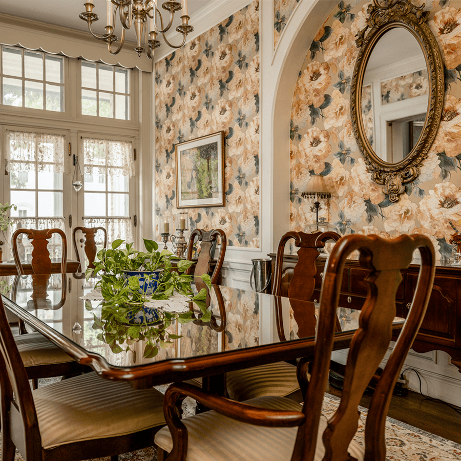 Dining room with floral wallpaper, wall mirror, buffet, horizontal table with matching chairs windows streaming in lights