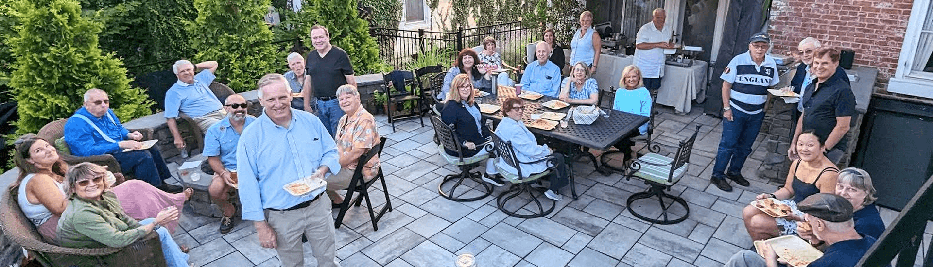 A group of people gather on a tiled patio, enjoying food, beverages and fellowship.