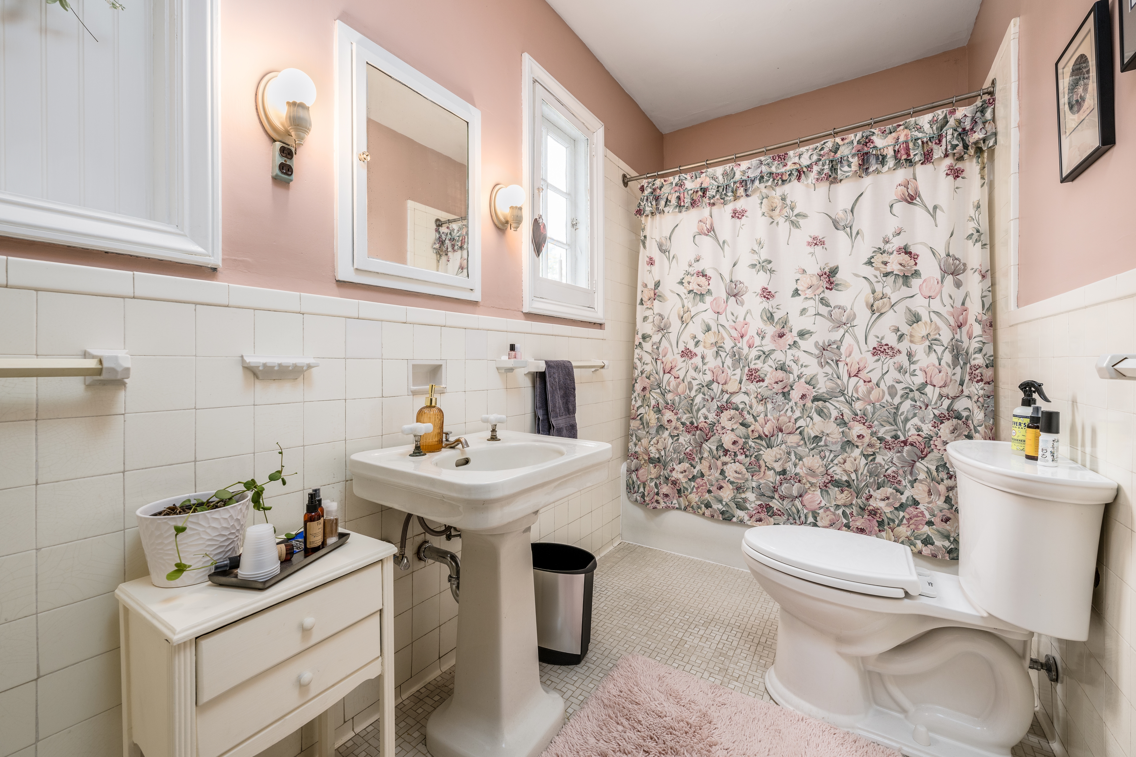 Shared bathroom with white tile, pink walls, and a floral shower curtain