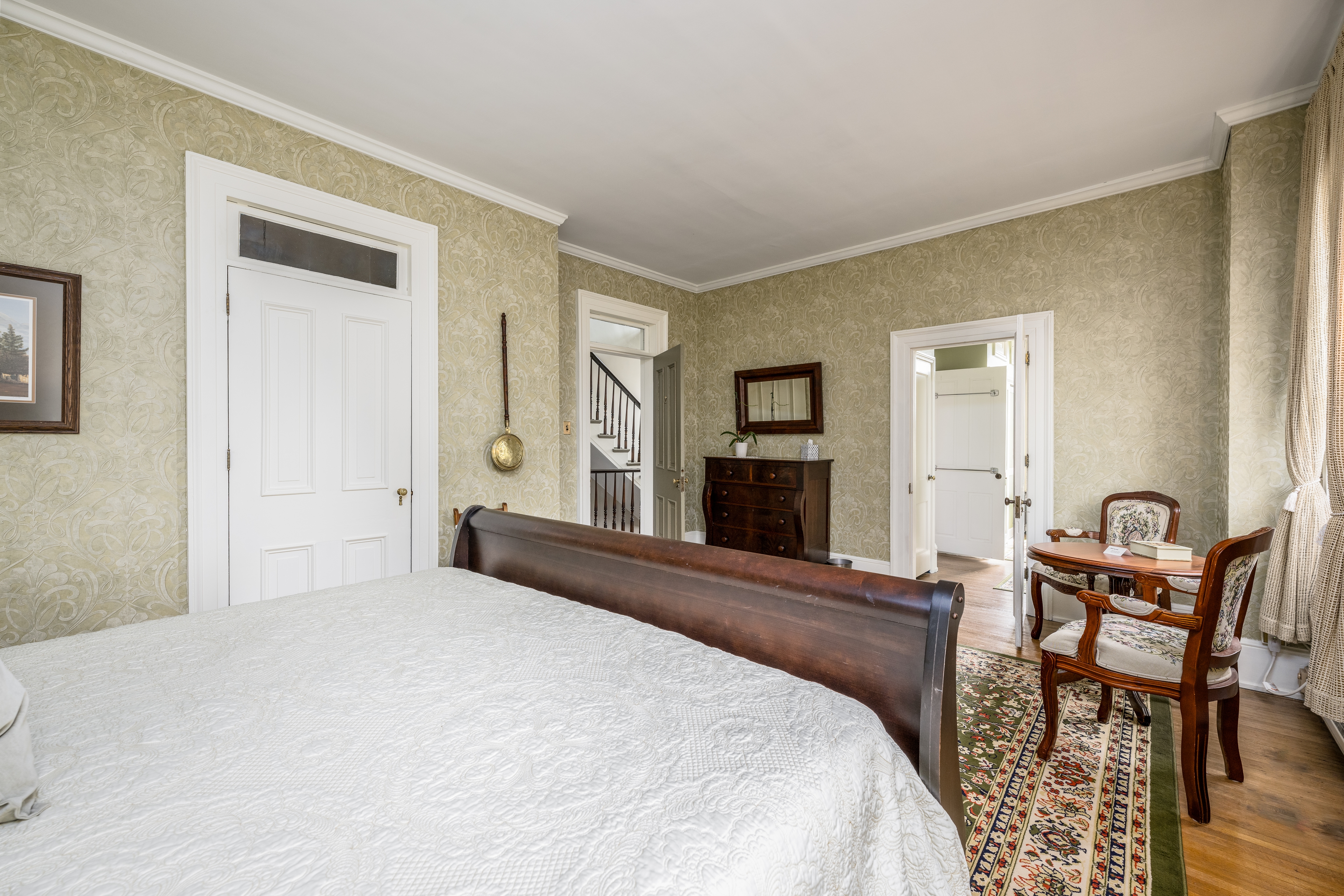 King bed with white comforter in the foreground, sleigh bed footboard and room with green wallpaper