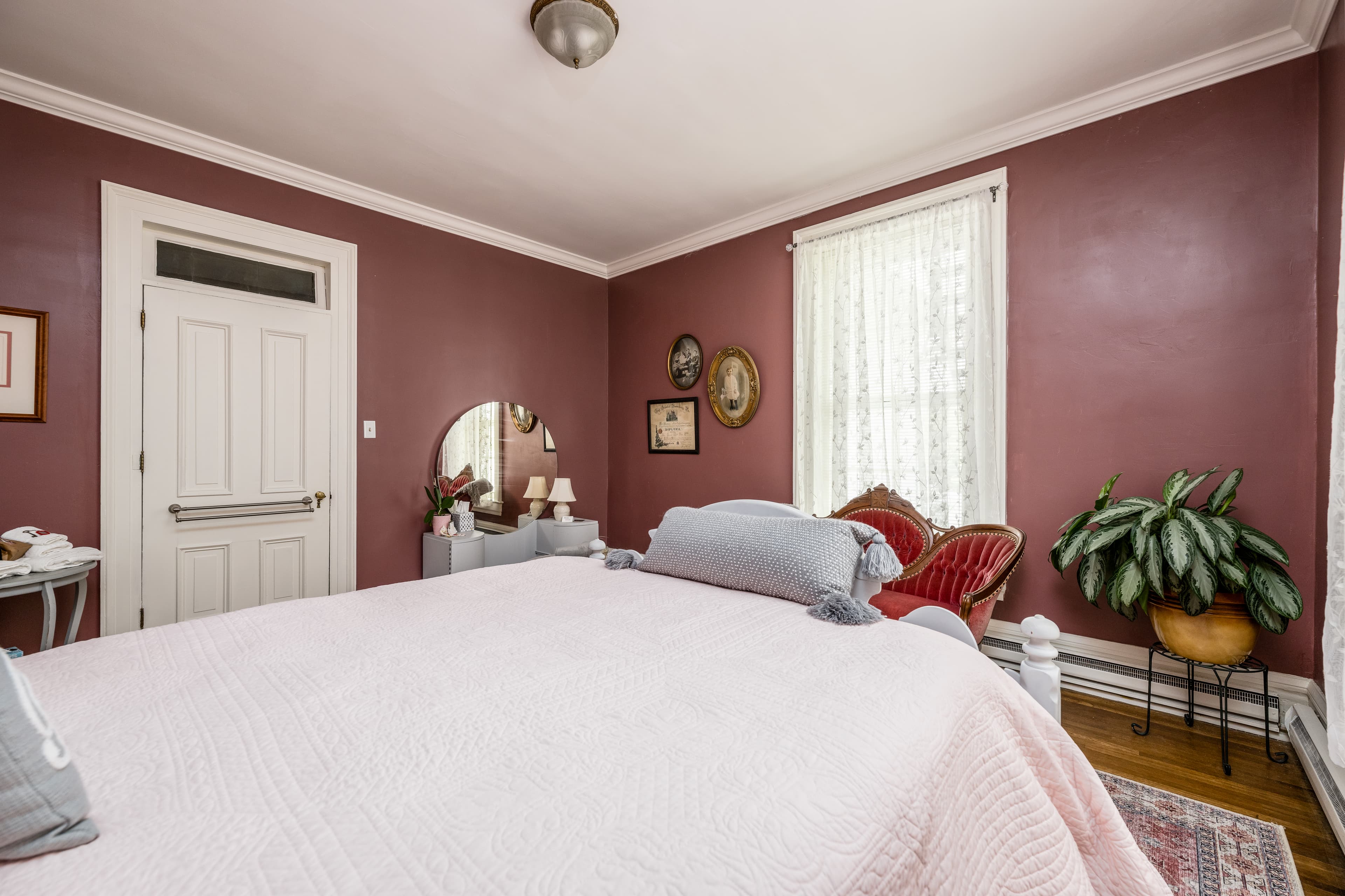 Queen bed with light pink comforter and a plant in the corner