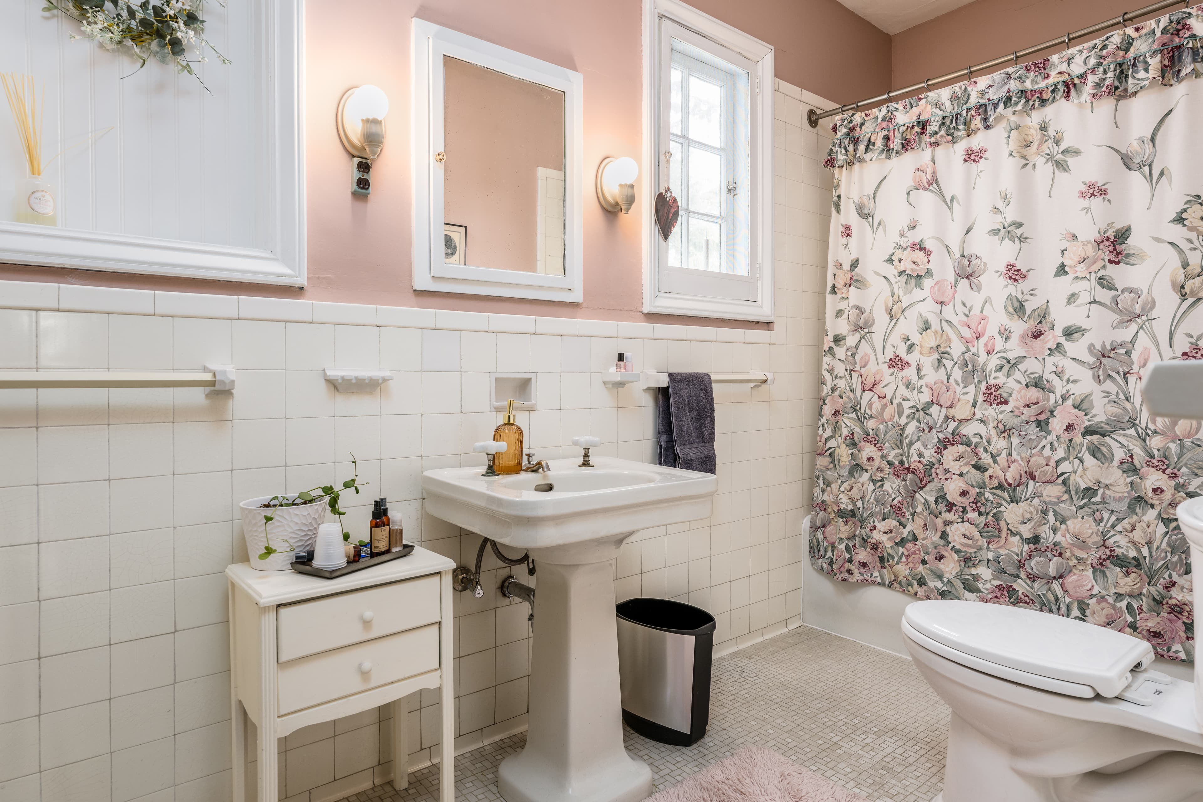 Shared bathroom with white tile, pink walls, and a floral shower curtain